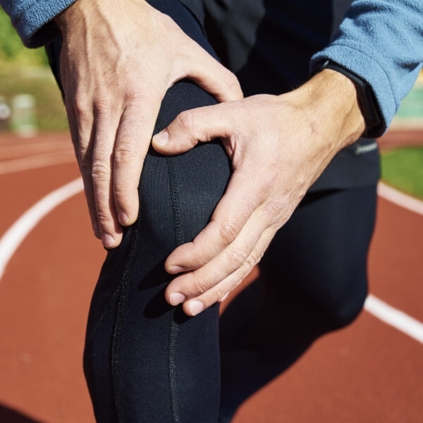 Male runner hands hold on his knee while running at stadium track, injury from running concept.